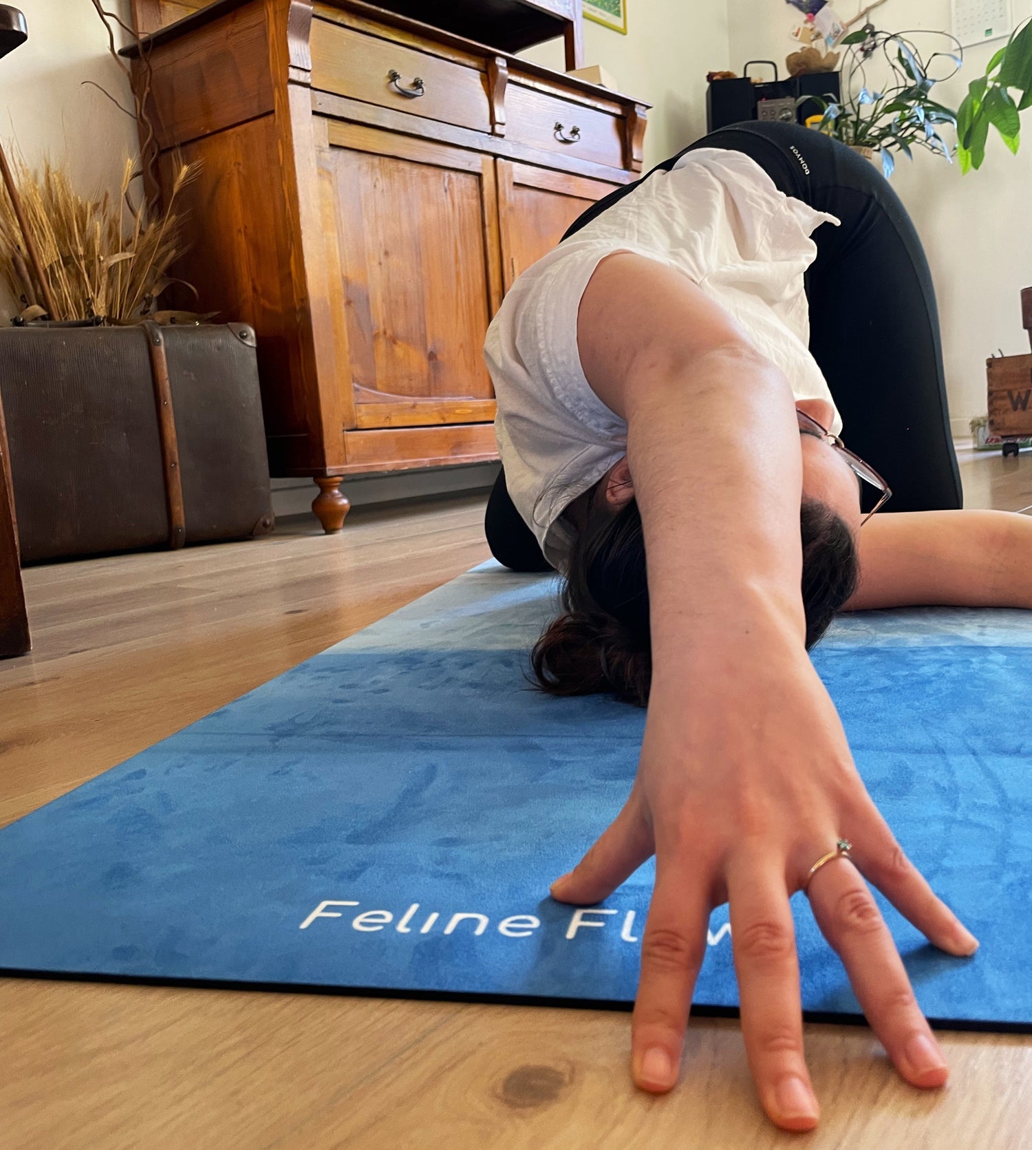 female stretching on blue yoga mat hand close up low angle Feline Flow brand